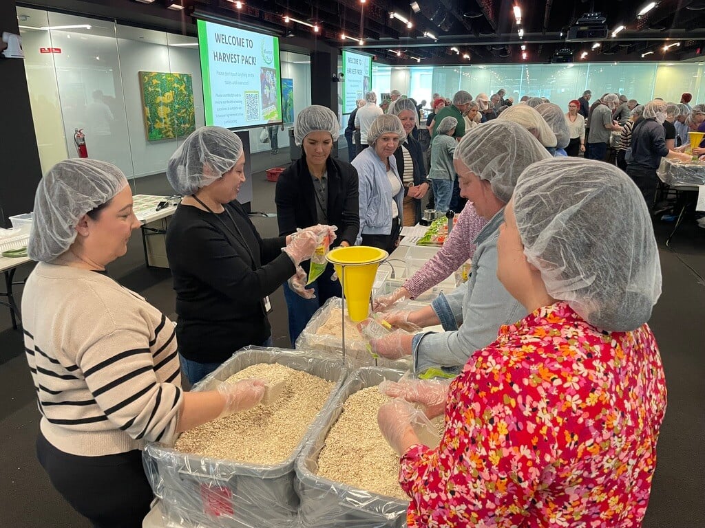 Employee volunteers smiling and engaging with each other while at their assembly line, packing meals.